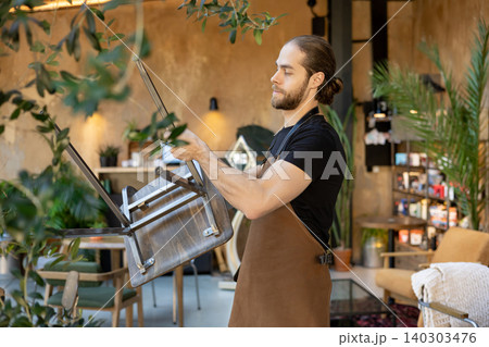 Male waiter organizing furniture and setting up cafe 140303476