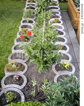 Multi-tiered round flowerbed made of concrete planters in the garden 140304446