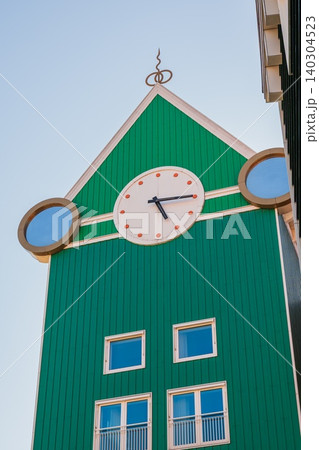 Large street clock on green wooden building facade, traditional dutch architecture design with round windows in Zaandam, contemporary real estate concept under clear sky, Netherlands Large street clock on green wooden building facade, traditional dutch architecture design with round windows in Zaandam, contemporary real estate concept under clear sky, Netherlands 140304523