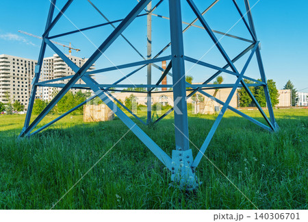 Steel electrical transmission tower base standing in grassy urban lot 140306701