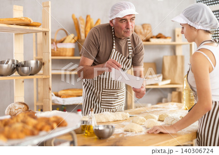 Male baker and teenage girl are looking at paper Male baker and teenage girl are looking at paper 140306724