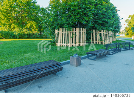 Park walkway with wooden benches, grassy lawn and fenced trees Park walkway with wooden benches, grassy lawn and fenced trees 140306725