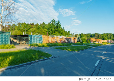 Suburban row of low brick garages along a quiet sunlit street 140306787