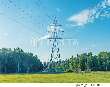 High-voltage transmission tower in green meadow near forest under blue sky High-voltage transmission tower in green meadow near forest under blue sky 140306809