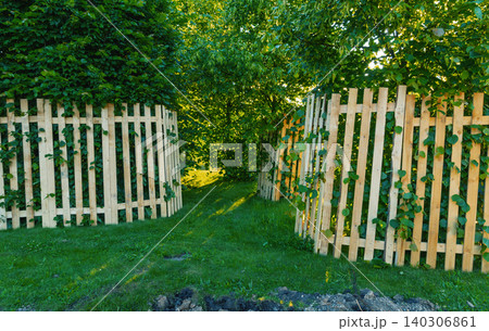 Wooden garden fence opening framed by lush green trees and vines 140306861