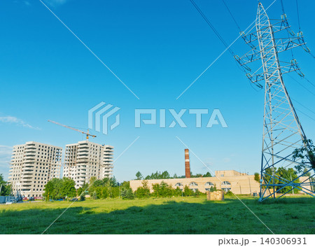 Urban construction site with power pylon and factory chimney under clear blue sky Urban construction site with power pylon and factory chimney under clear blue sky 140306931