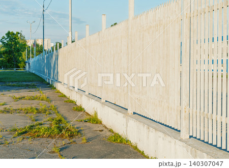 Long pale wooden slatted fence along cracked pavement with weeds Long pale wooden slatted fence along cracked pavement with weeds 140307047