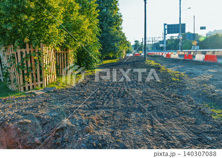Sunlit roadside excavation beside leafy suburban fence Sunlit roadside excavation beside leafy suburban fence 140307088