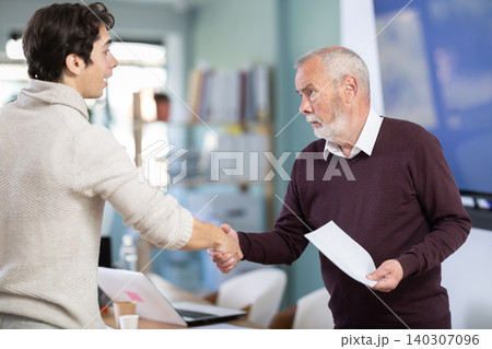 Smiling senior man makes deal, shaking hands with guy 140307096