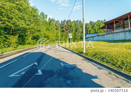 Empty suburban road curving past grassy embankment and forest Empty suburban road curving past grassy embankment and forest 140307318