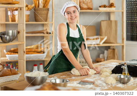 Teen girl works in bakery as baker, kneads dough, works with flour. Teen girl works in bakery as baker, kneads dough, works with flour. 140307322