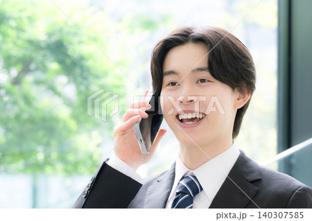 スマートフォンで顧客対応を行う若いビジネスマンのスーツの男性　営業やコミュニケーションイメージ 140307585