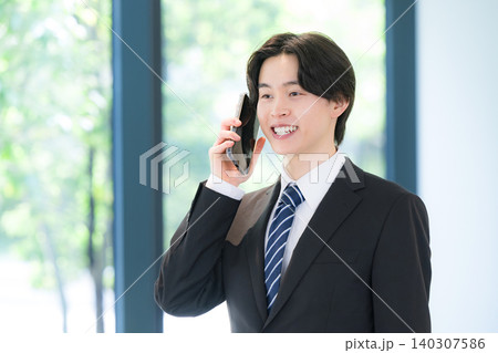 スマートフォンで顧客対応を行う若いビジネスマンのスーツの男性　営業やコミュニケーションイメージ 140307586