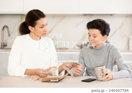 Mother giving some cash and instructions her teenager son sitting at home Mother giving some cash and instructions her teenager son sitting at home 140307784