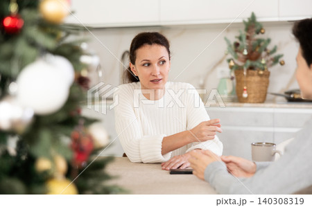 Mother and teenage son drinking tea in kitchen and chatting while celebrating Christmas 140308319