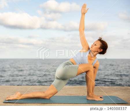 Yoga practice on embankment, female athlete fulfil carry out parivritta Anjaneyasana Yoga practice on embankment, female athlete fulfil carry out parivritta Anjaneyasana 140308337