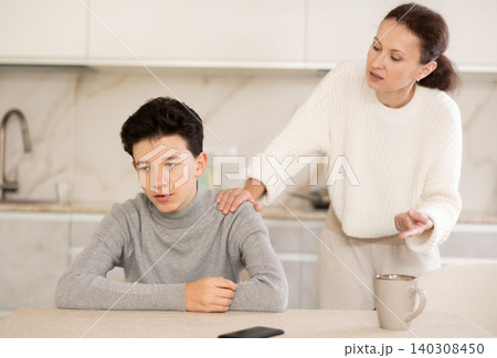 Portrait of offended boy sitting at home while mother berating him Portrait of offended boy sitting at home while mother berating him 140308450