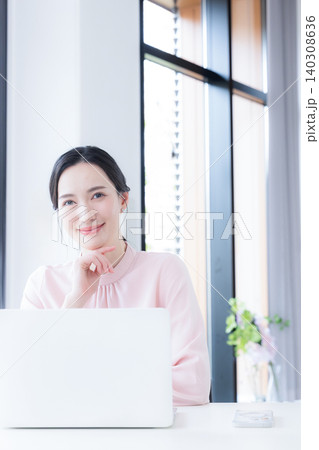 オフィスでデスクで座るパソコンの仕事をするピンクの服をカメラ目線美人な女性 オフィスでデスクで座るパソコンの仕事をするピンクの服をカメラ目線美人な女性 140308636