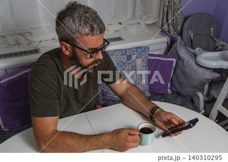 Enjoying morning coffee while checking phone in cozy home setting 140310295