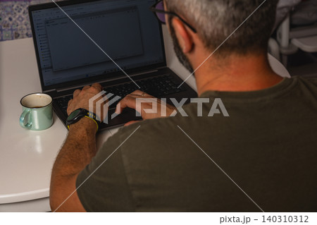 Man enjoys coffee while working on laptop at home during morning hours 140310312