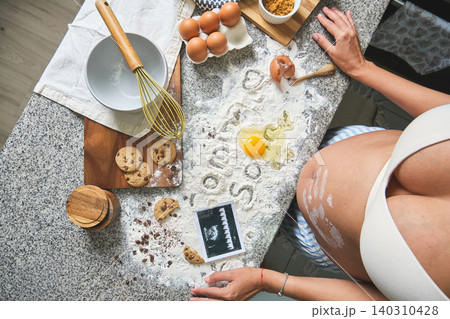 Pregnant woman baking cookies revealing pregnancy with sonogram Pregnant woman baking cookies revealing pregnancy with sonogram 140310428