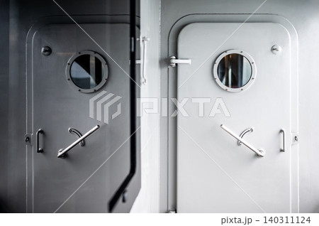 Heavy metal door with round porthole window and lever handle reflected in the mirror Heavy metal door with round porthole window and lever handle reflected in the mirror 140311124