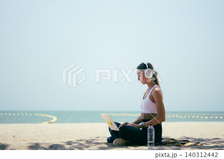 Side view of fit woman using laptop while sitting on the sand at a tropical beach 140312442