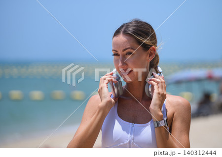 Young sporty woman with headphones getting ready for exercise by the sea. Young sporty woman with headphones getting ready for exercise by the sea. 140312444
