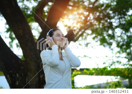 Woman enjoying music with headphones in park, uplifting wellness moment 140312451