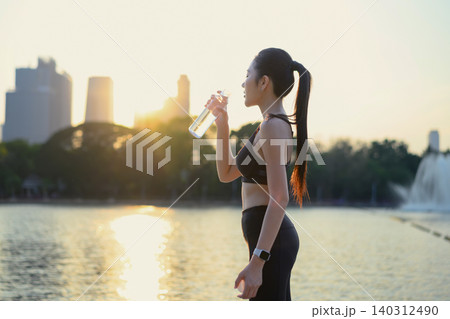 Woman drinks water after workout by lake at sunset Woman drinks water after workout by lake at sunset 140312490