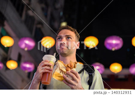 Handsome 30 years old Russian man tourist eating traditional bubble waffle and holding iced lemon tea at Temple Street Night Market in Hong Kong Handsome 30 years old Russian man tourist eating traditional bubble waffle and holding iced lemon tea at Temple Street Night Market in Hong Kong 140312931