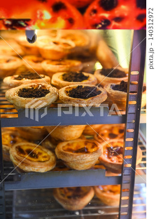 Traditional Macanese Portuguese egg tarts pastel de nata and chocolate topping tarts inside heated display showcase at local bakery shop in Macau 140312972