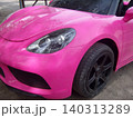 A close-up shot of the front quarter of a bright pink toy electric sports car. It features detailed black headlights, a realistic rubber tire with a black rim, and a molded plastic bumper. 140313289
