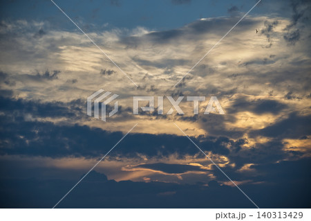 Dramatic sunset sky with layered clouds and a distant bird soaring high 140313429