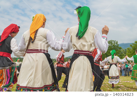 Women in Bulgaria costumes perform hora dance during folk festival with dancers holding hands outdoors. Hora dance, Bulgarian culture concept, cultural expression, traditional dance celebration Women in Bulgaria costumes perform hora dance during folk festival with dancers holding hands outdoors. Hora dance, Bulgarian culture concept, cultural expression, traditional dance celebration 140314823