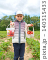 Full length portrait of a young boy standing in an open agricultural field, holding a clear plastic bucket and a white wicker basket full of ripe red strawberries in daylight 140315433