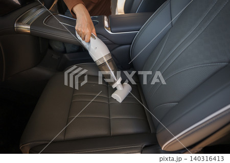 close up hand of woman using portable handheld vacuum cleaner to clean dust on leather car seat of electric car close up hand of woman using portable handheld vacuum cleaner to clean dust on leather car seat of electric car 140316413