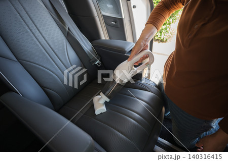 close up hand of woman using portable handheld vacuum cleaner to clean dust on leather car seat of electric car close up hand of woman using portable handheld vacuum cleaner to clean dust on leather car seat of electric car 140316415