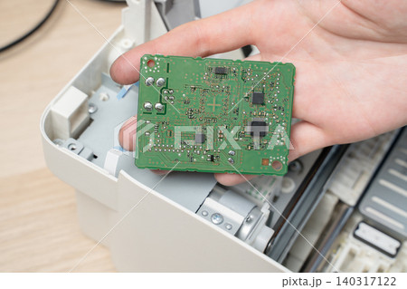 Hand Holding Green Circuit Board Inside Disassembled Printer During Electronics Repair And Maintenance Hand Holding Green Circuit Board Inside Disassembled Printer During Electronics Repair And Maintenance 140317122