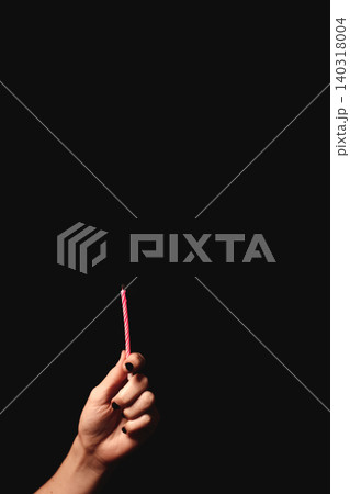 Hand holding a pink striped candle against dark background 140318004
