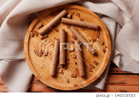 Crispy wafer rolls filled with chocolate cream served on a rustic bamboo plate over a textured cloth. Crispy wafer rolls filled with chocolate cream served on a rustic bamboo plate over a textured cloth. 140318583