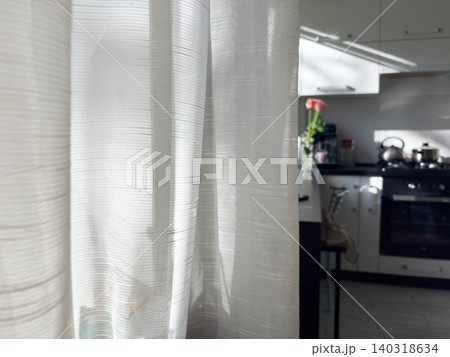 the delicate texture of white ribbed sheer curtains overlooking a modern kitchen design. Natural light suggests a sunny morning, creating a clean, airy, and peaceful domestic atmosphere. the delicate texture of white ribbed sheer curtains overlooking a modern kitchen design. Natural light suggests a sunny morning, creating a clean, airy, and peaceful domestic atmosphere. 140318634