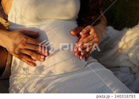 Hands Embracing Pregnant Belly in Warm Sunlight 140318793