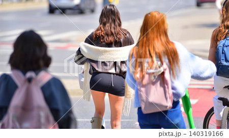 View of girls on electric scooters waiting for the green light at a pedestrian crossing. View of girls on electric scooters waiting for the green light at a pedestrian crossing. 140319166