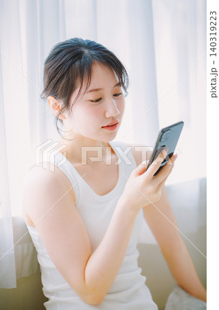 窓辺でスマホを見る若い女性 窓辺でスマホを見る若い女性 140319223