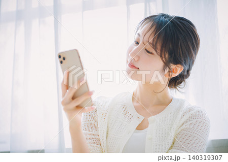 窓辺でスマホを見る若い女性 140319307