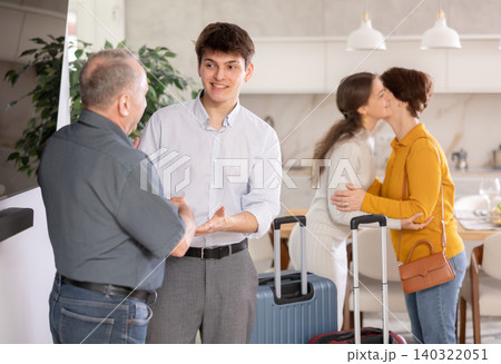 Young guy with suitcase coming back home, father welcoming son at door. Parents happy to see home, welcoming children Young guy with suitcase coming back home, father welcoming son at door. Parents happy to see home, welcoming children 140322051