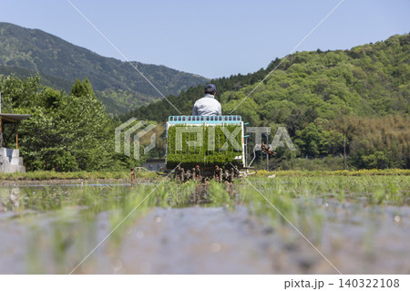 新緑の山々に囲まれた水田で田植えをする農家 新緑の山々に囲まれた水田で田植えをする農家 140322108