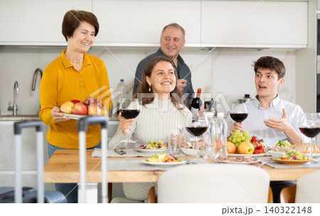 Smiling young guy with girlfriend visiting parents. Young sitting with glasses of wine at family table Smiling young guy with girlfriend visiting parents. Young sitting with glasses of wine at family table 140322148