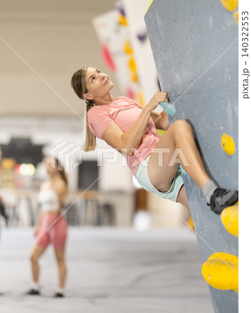 Woman climbs artificial wall bouldering, working out in gym Woman climbs artificial wall bouldering, working out in gym 140322553